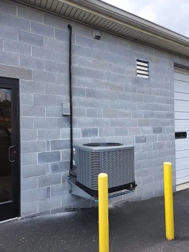 Condensing unit on a wall-mounted bracket outside a block commercial building with bollard protection